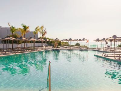 Large clear pool with lounge chairs and umbrellas on a sunny day.
