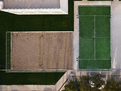 Vista drone di due campi sportivi adiacenti, uno sabbioso e uno in erba artificiale verde.