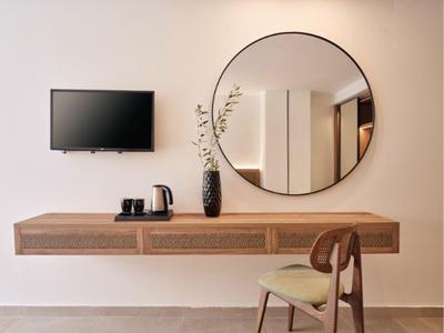 Modern living area with wall mirror, wooden table, chair, and TV mounted on wall.
