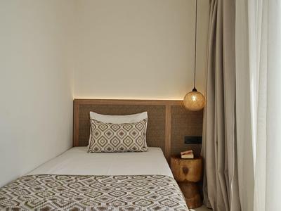 Single bed in a hotel room with patterned bedding, decorative pillow, and hanging lamp.