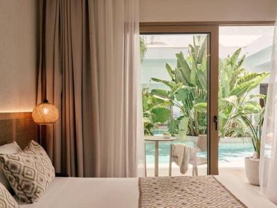 Modernes Hotelzimmer mit großem Bett und Blick auf einen Pool und tropische Pflanzen.