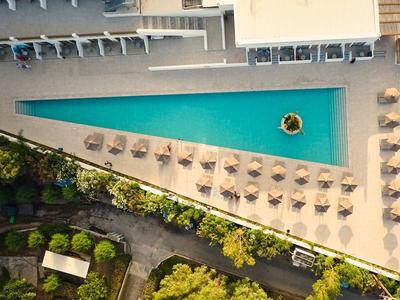 Dreieckiger Hotelpool mit Sonnenschirmen auf einer Terrasse, umgeben von grünen Bäumen.