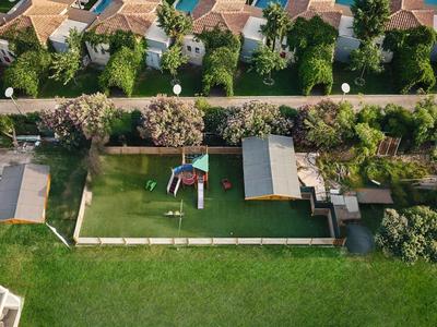 Grünes Grundstück mit Spielplatz und Gebäuden in Wohngegend neben Häusern mit roten Dächern.