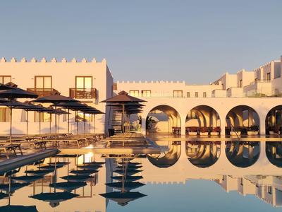 Hotelpool mit Sonnenliegen und weißen Gebäuden bei Sonnenuntergang.