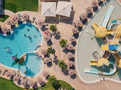 Zwei Schwimmbereiche: ein Herz-förmiger Pool mit Liegestühlen und ein Wasserspielplatz mit Rutschen.