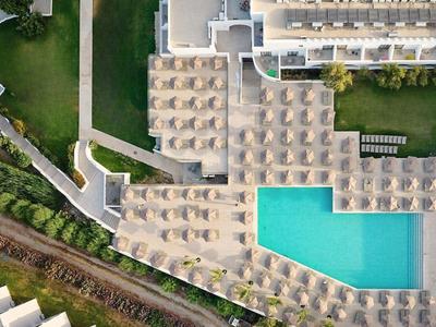 Vogelperspektive eines Hotels mit Pool und Liegestühlen umgeben von Grünflächen.