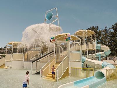 Große Wasserrutsche in einem Außenpool mit spielenden Kindern und Bäumen im Hintergrund.