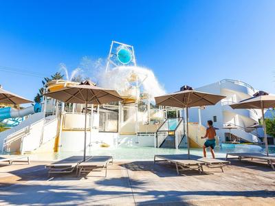 Outdoor pool area with sun loungers, umbrellas, and a water slide under a clear blue sky.