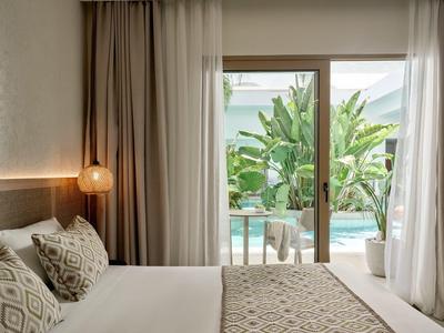 Modern hotel bedroom with double bed and sliding door overlooking pool and greenery.