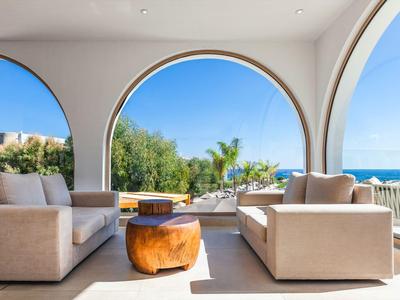 Zona living moderna con due divani davanti a grandi archi con vista su giardino e mare.