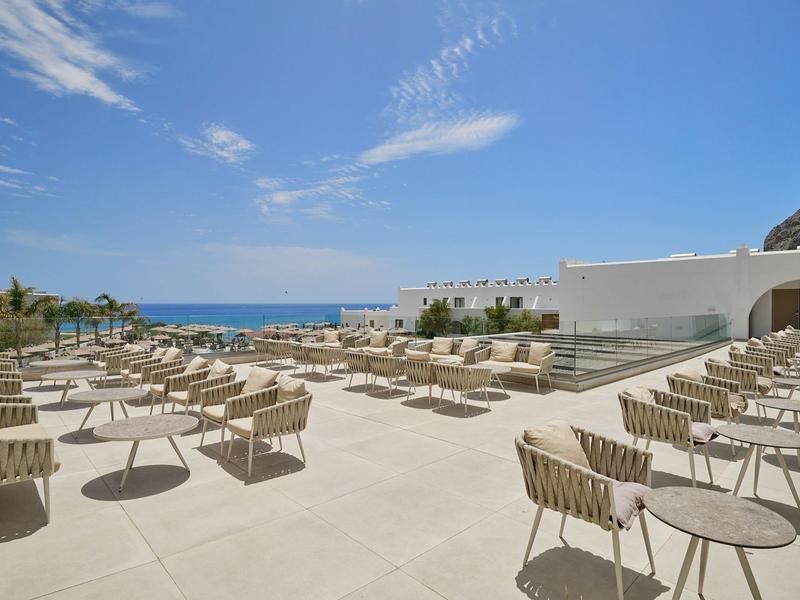 Spacious outdoor seating area with chairs and tables overlooking the ocean under a blue sky.