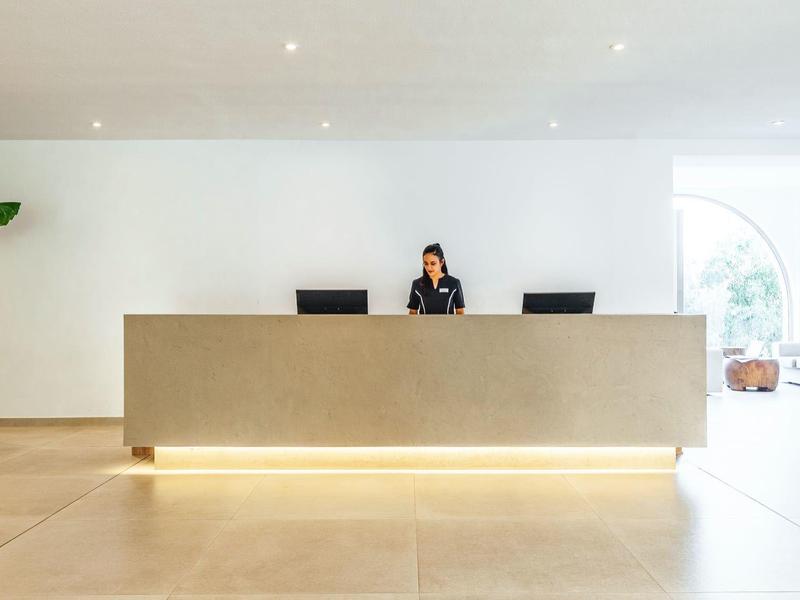 Modern hotel reception with a beige desk, receptionist, and bright minimalist interior.