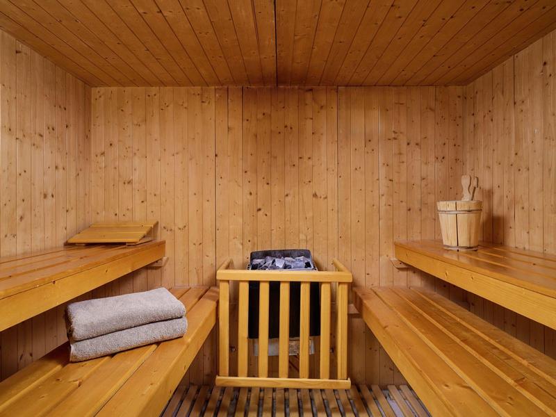 Cozy wooden sauna room with benches, towels, and sauna stove with bucket and ladle.