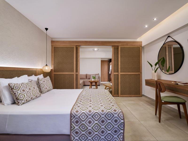 Modern hotel room with a large bed, patterned runner, wooden furniture, and a round mirror.