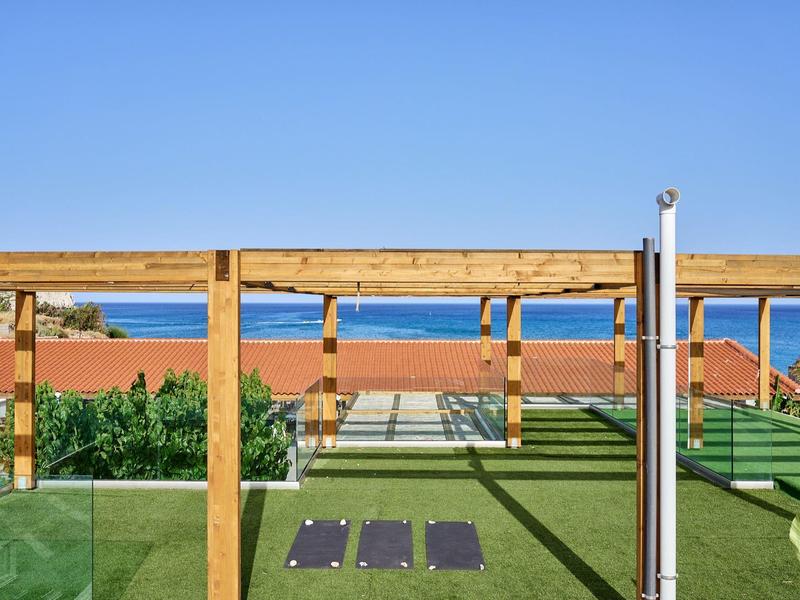 Roof terrace with sunbeds, wooden pergola, and a sea view under a clear blue sky.