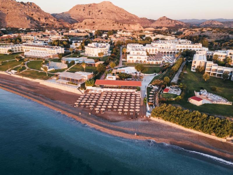 Beach resort with sun loungers on sandy beach in front of white hotels and mountains behind.