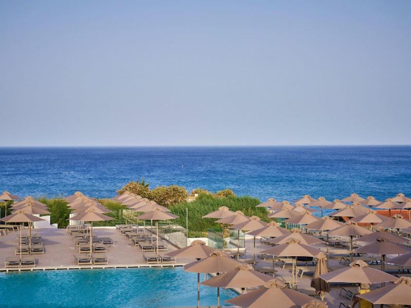View of a pool area with multiple sun loungers and umbrellas by the sea.