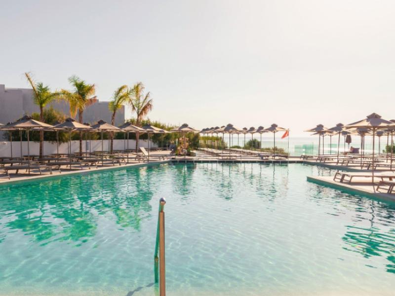 Large clear pool with lounge chairs and umbrellas on a sunny day.