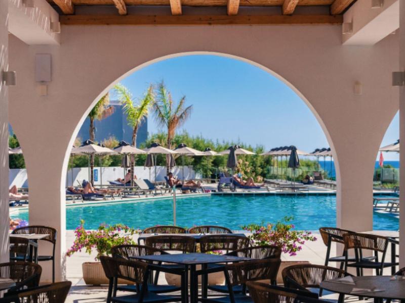 View through an archway of a pool with lounge chairs and palm trees on a sunny day.