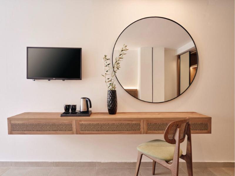 Modern living area with wall mirror, wooden table, chair, and TV mounted on wall.