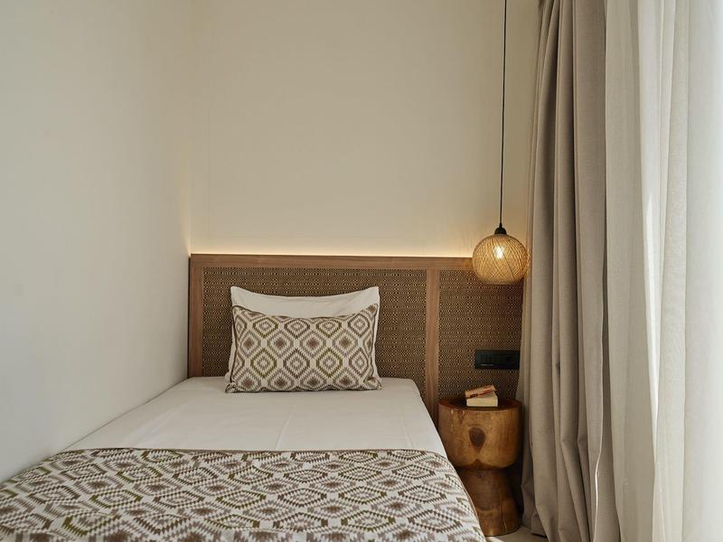 Single bed in a hotel room with patterned bedding, decorative pillow, and hanging lamp.