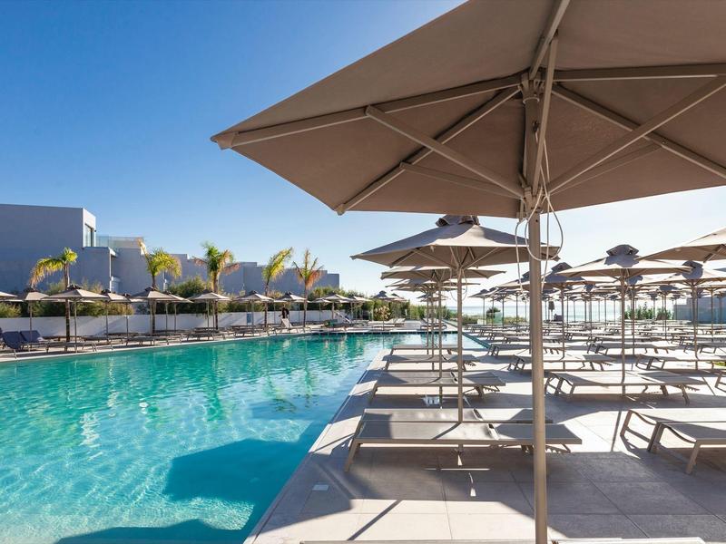 Outdoor pool area with large umbrellas and lounge chairs under clear blue sky.