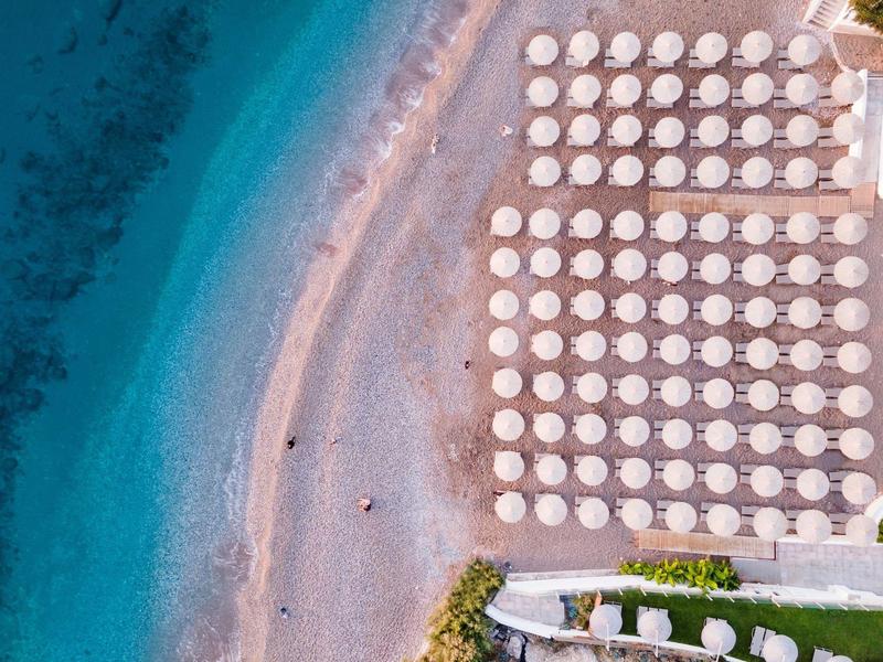 Aerial view of a beach with rows of white umbrellas and turquoise water.
