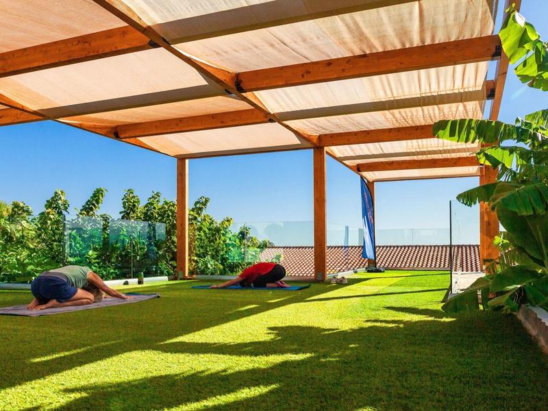 Outdoor yoga area with grass and wooden pergola under clear blue sky.