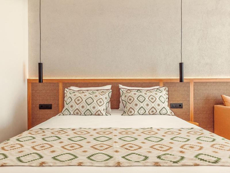 Modern hotel room with a double bed, geometric patterned bedding, and pendant lights.