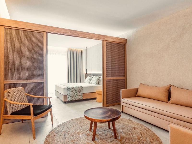 Cozy hotel suite with a brown sofa, armchair, round wooden table, and a bed in the background.