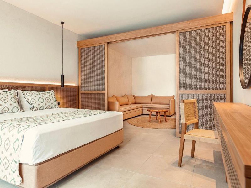 Modern hotel room with a double bed and separate seating area with sofa and table.