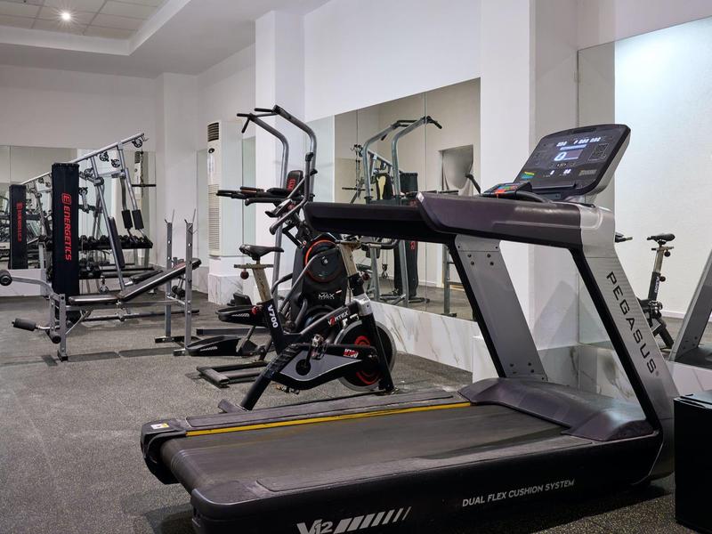 Modern hotel gym with treadmill, exercise bike, weight machine, and mirrored walls.