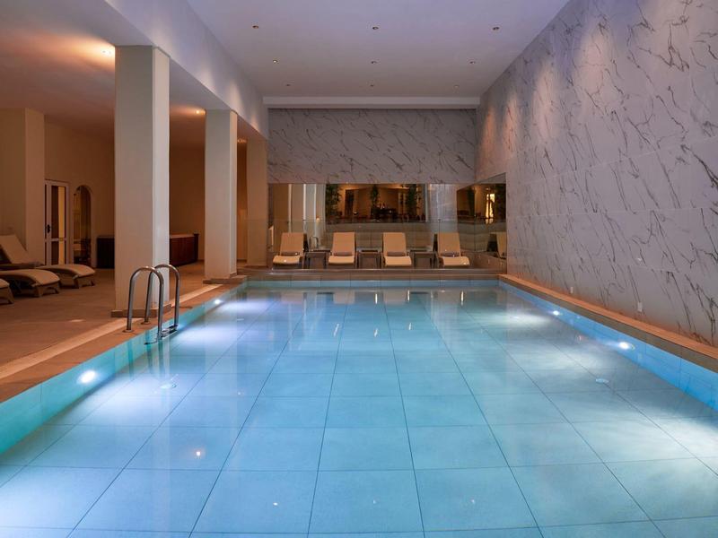 Indoor pool with lounge chairs and marble wall, softly lit for relaxation.