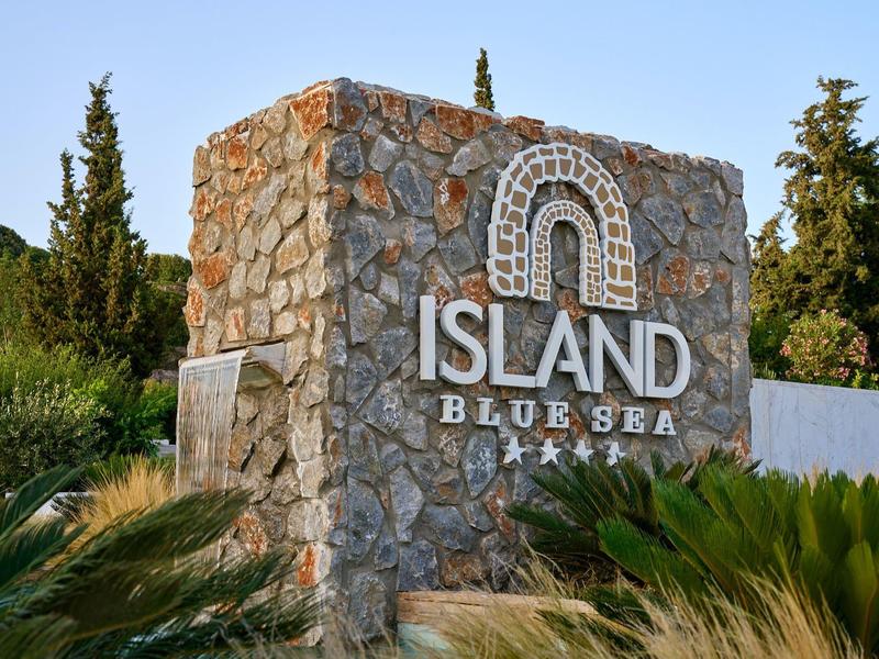 Stone monument with ISLAND BLUE SEA sign surrounded by greenery under clear sky