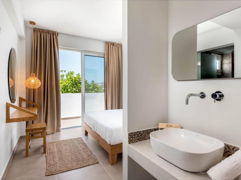 Bright, modern hotel room with bed, desk, balcony, and elegant sink area.