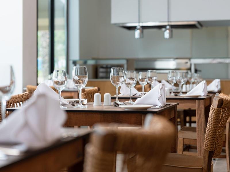 Modern restaurant with set tables and rattan chairs.