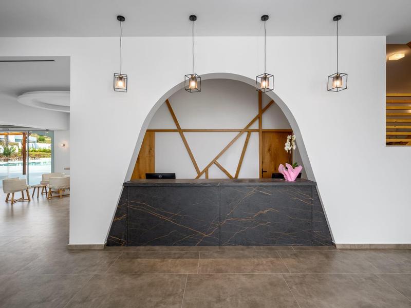 Modern hotel lobby with black reception desk, hanging lights, and architectural wall decor.