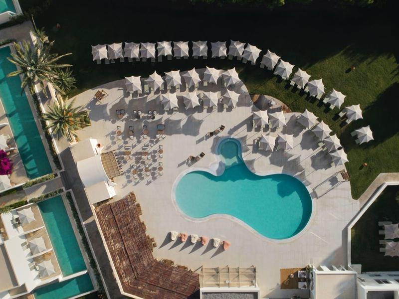 Aerial view of a hotel pool area with sunbeds and green lawns around.