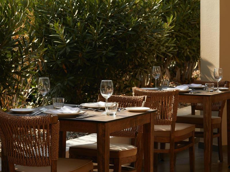 Cozy outdoor terrace with wooden tables and chairs set with wine and water glasses.