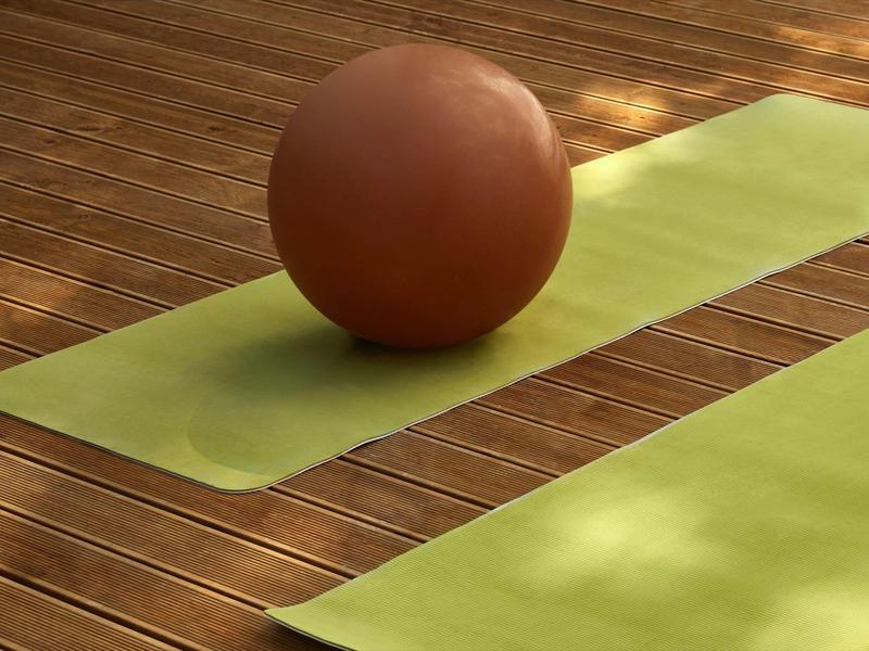 A brown exercise ball rests on a green yoga mat on a wooden floor.