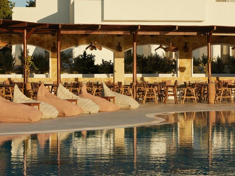 Comfortable bean bags by the pool under a wooden pergola with tables and chairs in the background.