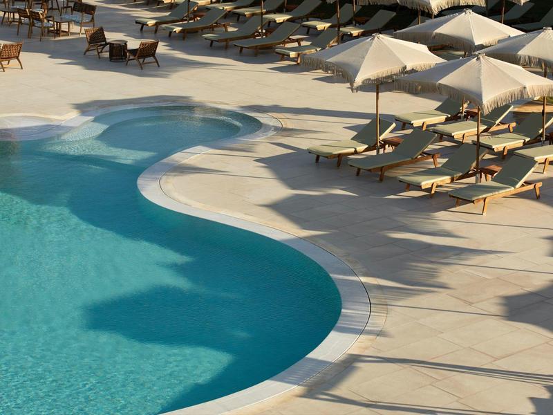 Curved hotel pool with lounge chairs and umbrellas on light stone floor
