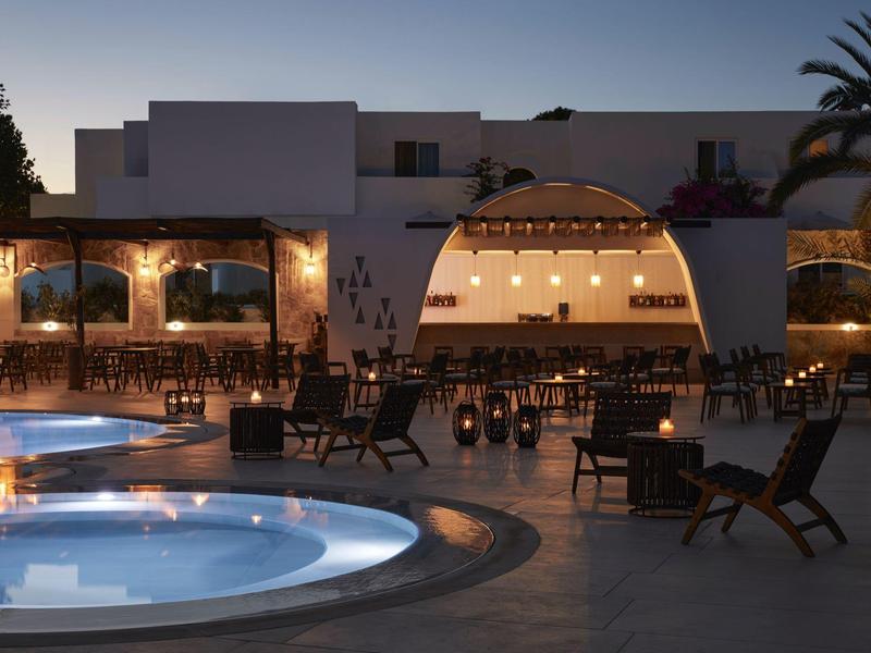 Evening view of a hotel with illuminated pool and outdoor seating area.