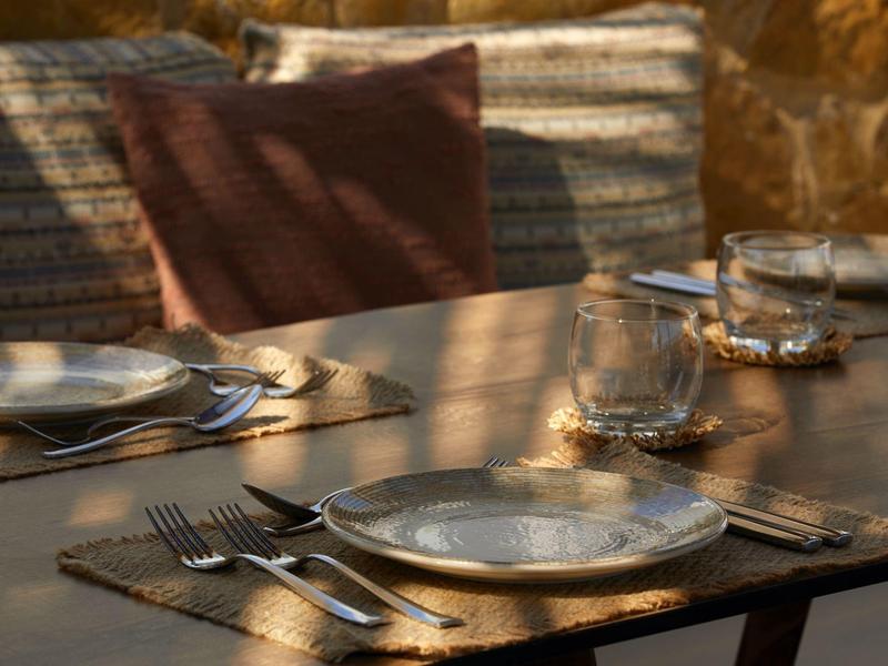 Outdoor table set with plates, cutlery, and glasses in front of a cushioned bench.