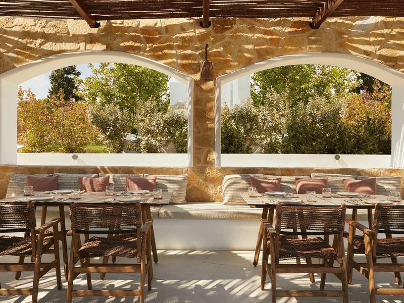 Cozy outdoor area with wooden chairs and cushioned benches under a stone roof.