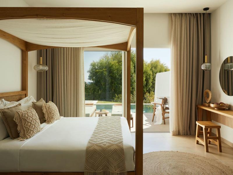 Bright bedroom with canopy bed and view of terrace and pool.