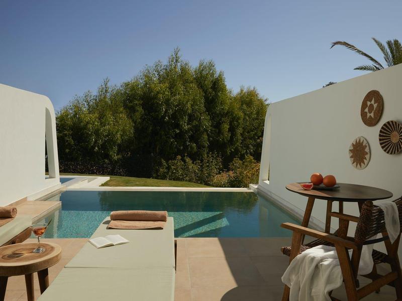 Modern outdoor area with pool, white walls, and wooden furniture under blue sky.