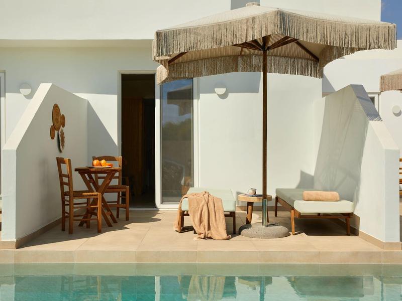 Terrace with wooden chair, table, lounge chair, and umbrella next to a pool on a sunny day.
