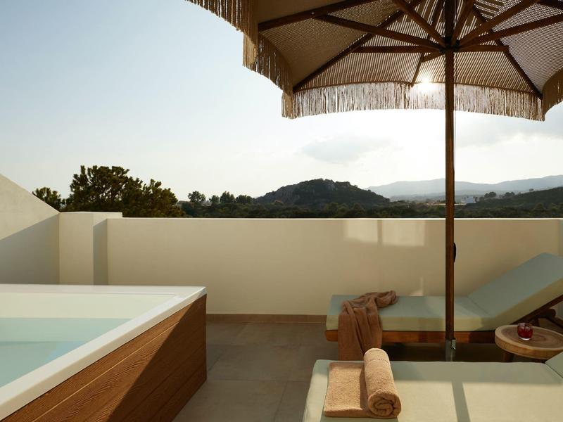 Modern outdoor area with bathtub, sun umbrella, and mountain view at sunset.