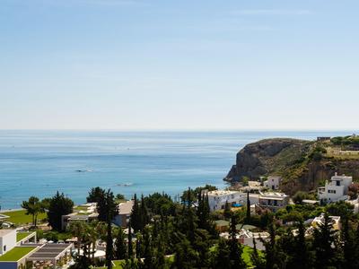 Paisaje costero con vista al mar, acantilados y edificios blancos entre árboles verdes.